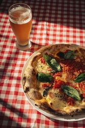 Margherita pizza with basil and tomato served with cold beer on checkered tablecloth