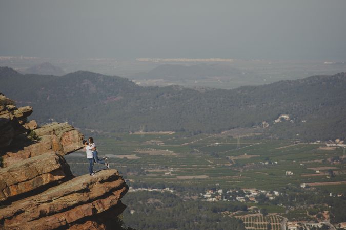 Distant loving couple embracing while standing on high cliff