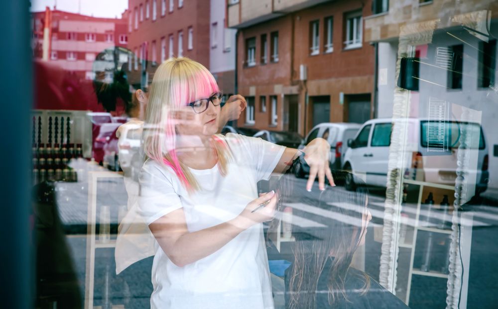 Hairdresser styling hair, seen through reflection in window