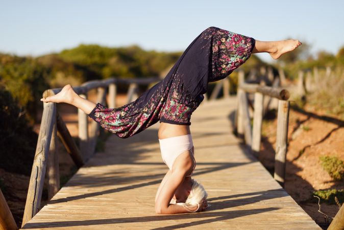 Woman practicing headstand in yoga pose on wooden bridge