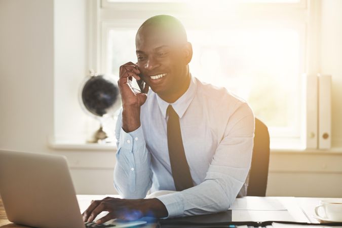 Man in suit and tie smiling on phone while working at his desk