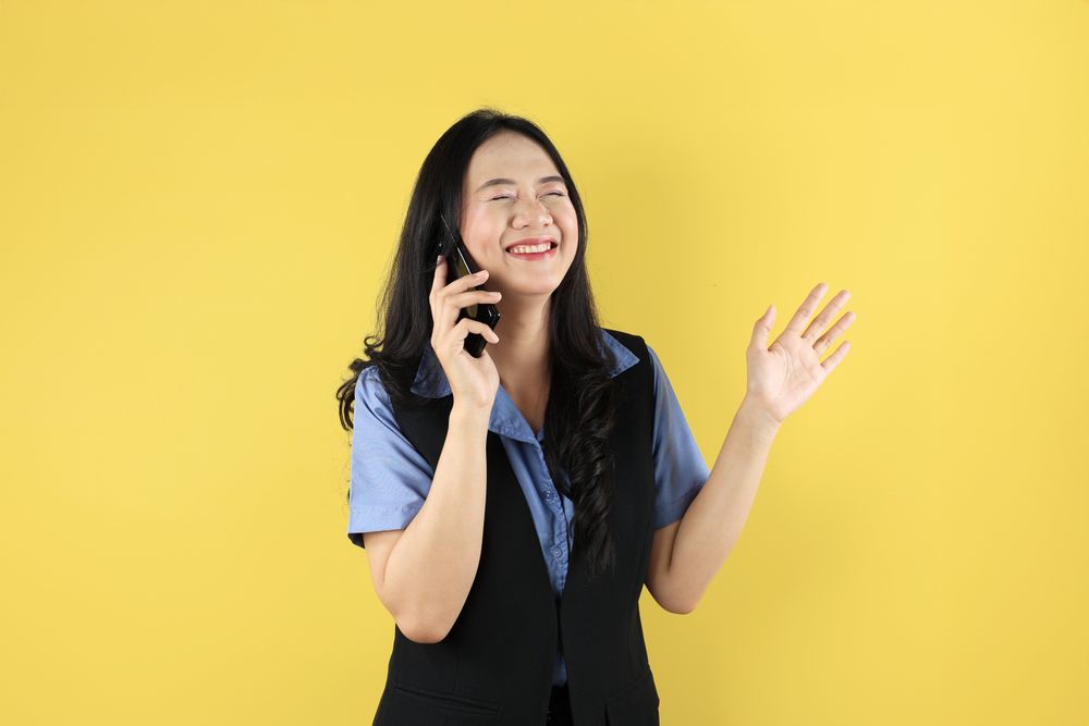 Young Asian Woman Making a Call Using a Cell Phone With Eye Closed, Happy Smiling Gesture.