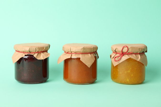 Glass jars with jam on mint background, space for text