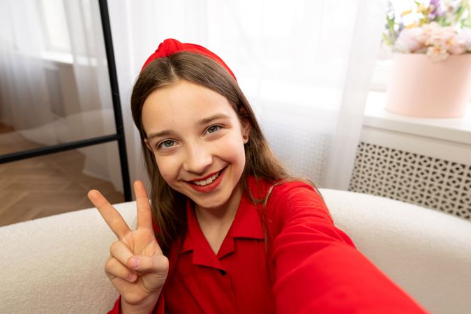 Close-up selfie of smiling teen girl showing peace gesture.