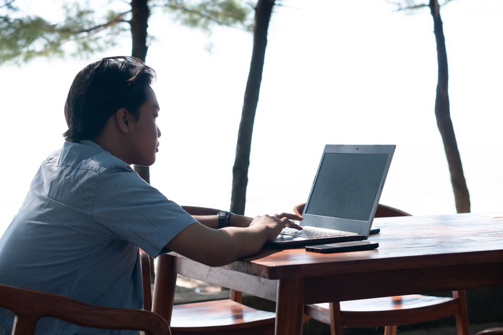 Back View Asian Young businessman work at outdoor with laptop blank screen. Concept of remote and freelance work. Young successful man wearing casual blue cloth.