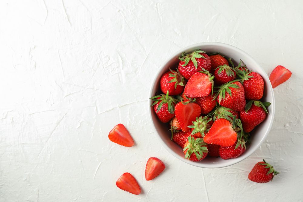 Bowl with fresh strawberries on light background, space for text. Summer sweet fruits and berries