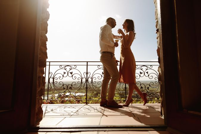 Ground level shot of a couple standing in the balcony holding wine