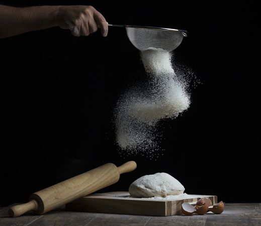 Cropped image of hand putting flour on dough
