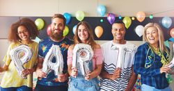 Friends standing with silver balloons reading “party”