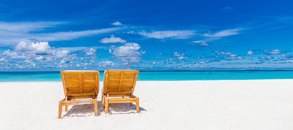 Two lounge chairs on an empty tropical beach with light sand