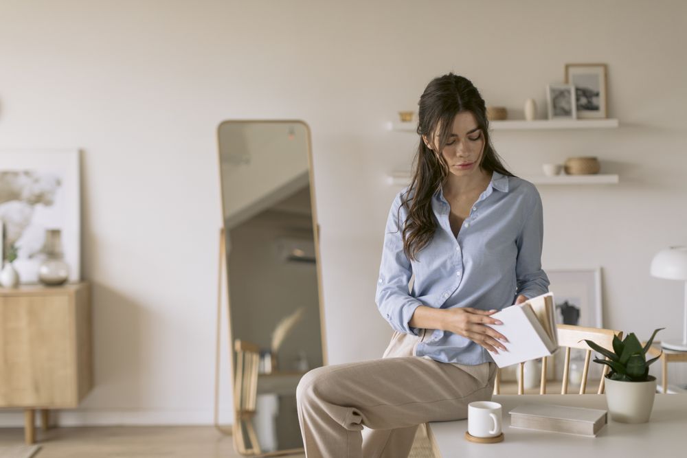 Woman sitting on top of a table while looking through a book