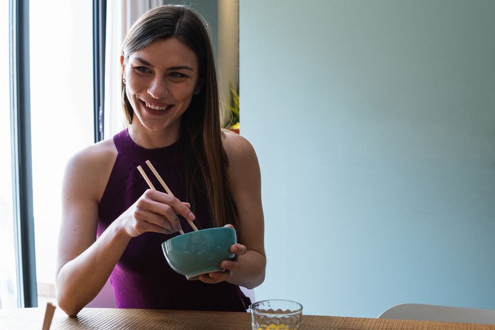 Cheerful woman with chopsticks having lunch in dining room