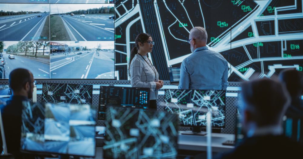 Advanced City Planning Monitoring Center with Diverse Male and Female Officers Analyzing CCTV Footage, Traffic Data and Road Situation on a Big Digital Screen.