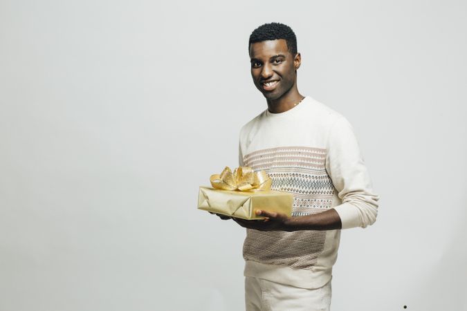 Smiling Black man holding a gold present with a bow in a bright room