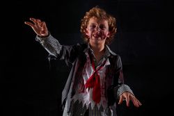 Child disguised as a zombie with blood and glitter with arms raised walking with an expression of anger