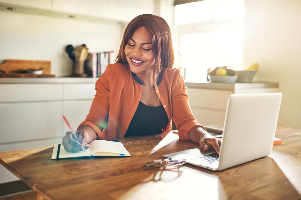 Businesswoman smiling while taking notes from her laptop