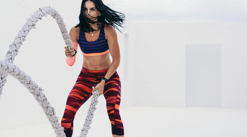Slender fit woman using battle ropes to workout