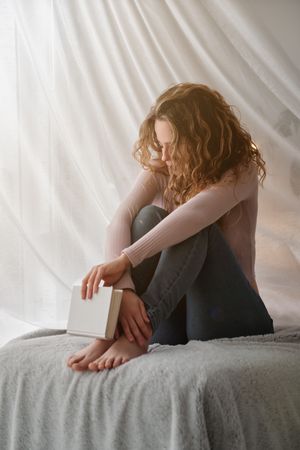 woman sitting on bed and holding book in light room