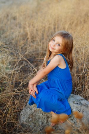 Female child sitting on bolder in field, vertical