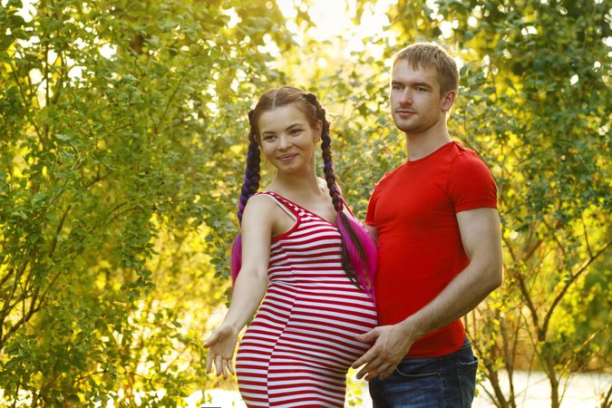 Pregnant woman reaching ahead with her partner in a sunny park