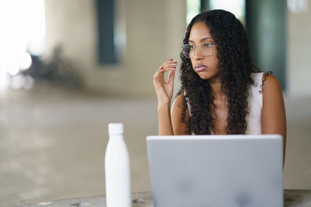A Contemplative Woman Who is Diligently Working on Her Laptop in a Modern Workplace Environment