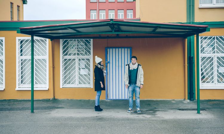 Happy couple wearing winter clothes standing under a metallic roof outdoors in a cold and rainy day