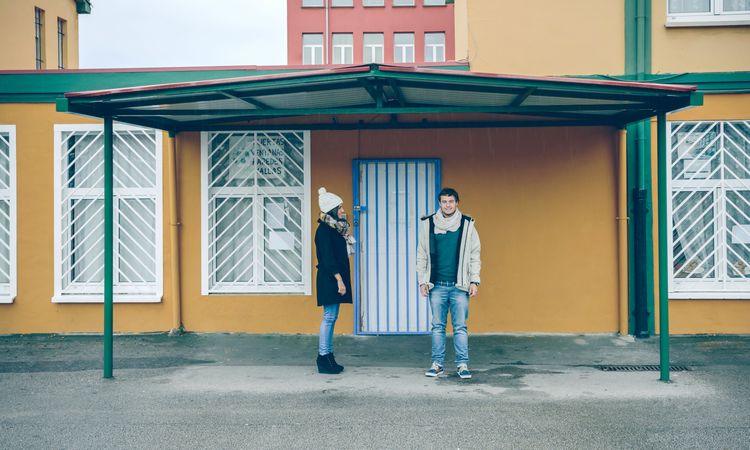 Happy couple wearing winter clothes standing under a metallic roof outdoors in a cold and rainy day