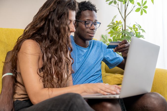 A young man looks lovingly at his partner while she is focused on her smartphone, a moment of quiet affection.