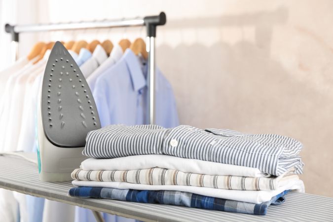 Iron and stack of shirts on ironing board, space for text