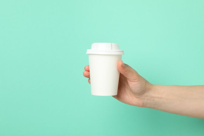 Female hand holds paper cup on mint background, space for text