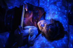 Boy resting on bed with gadget in neon lights