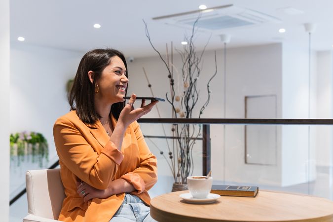 Delighted woman recording audio message on smartphone