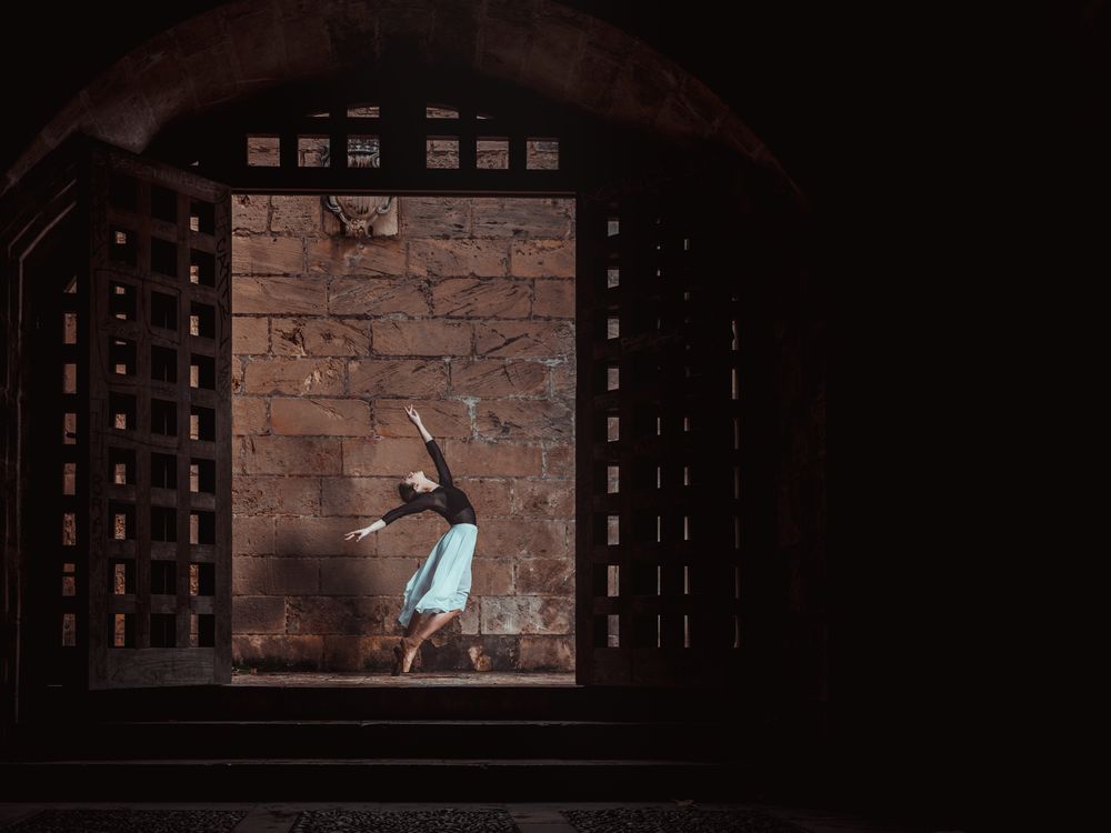 Female ballet dancer dancing in dark passage near stone wall