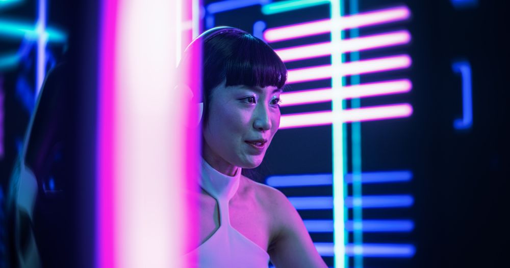 Portrait of a Stylish Asian Streamer or Gamer in Chats with Internet Subs on Computer in Futuristic Neon Room.