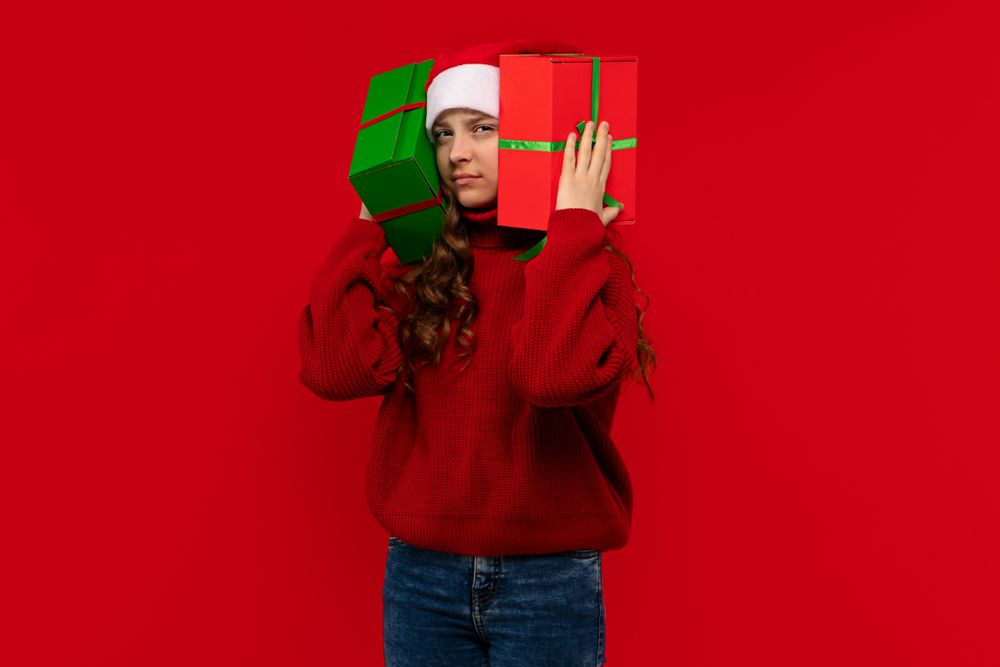 Girl in Santa hat holds Christmas presents to her ears