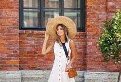 Woman adjusting her straw hat outside a brick building