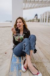 Content woman eating salad from plastic bowl sitting on wooden terrace