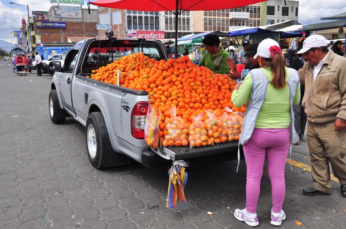 People buying oranges from a pickup truck at the street market