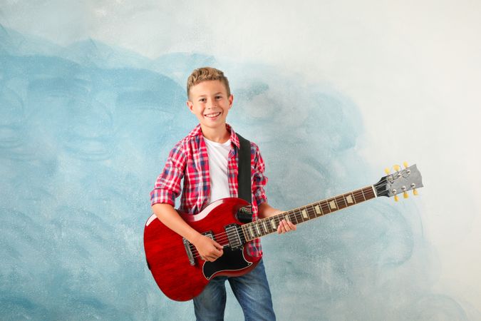 Happy boy with electric guitar on color background, space for text
