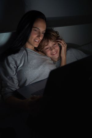 Delighted boy with mother browsing laptop in darkness