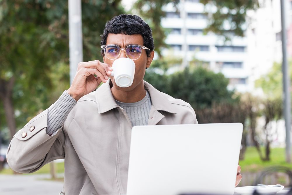 Focused hispanic man using laptop and drinking coffee