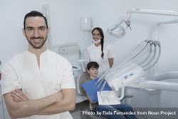 A portrait of a smiling dentist with his team smiling with teenage patient in the background bxZMM5