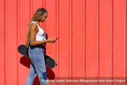 Woman walking in front of red wall with phone and skateboard 5aQk85