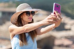 Positive woman in hat taking selfie on smartphone while standing on street