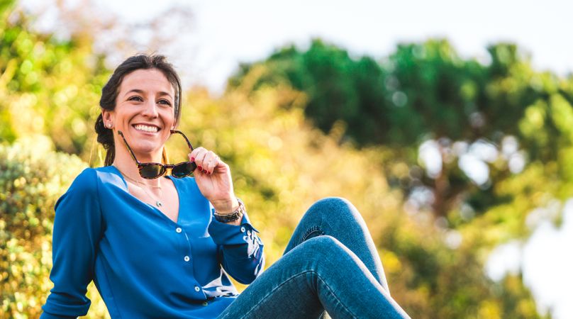 portrait of young woman with sunglasses sitting on grass in park