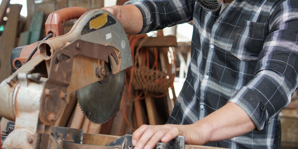 Hand of carpenter using electric circular saw cutting wood board at the carpentry workshop