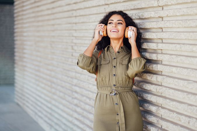 Middle eastern woman listening on headphones while wearing green jumpsuit outside
