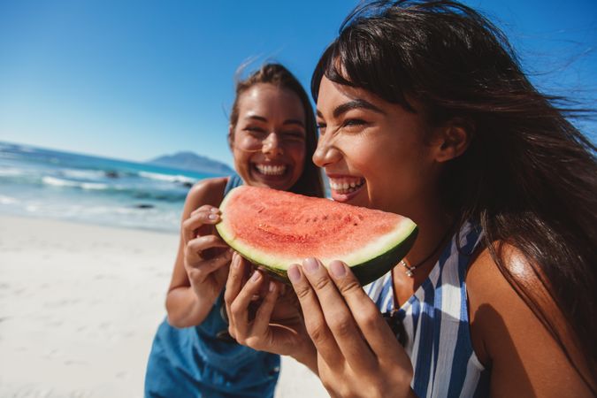 Cheerful female friends sharing fruit on the beach