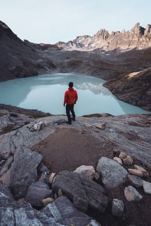 Back view of man in red jacket standing near frozen lake