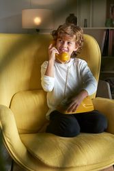 Cheerful boy speaking on telephone in armchair